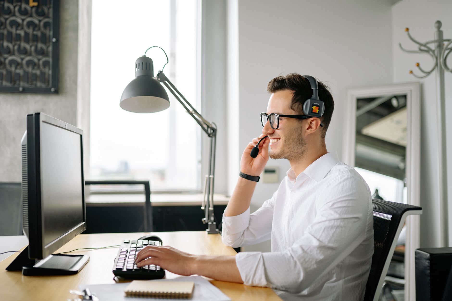 Smiling man wearing headset working at computer in bright office — illustrating: Best VoIP Services for Central Florida Businesses: Price, Features & HIPAA Compliance Compared (2024)